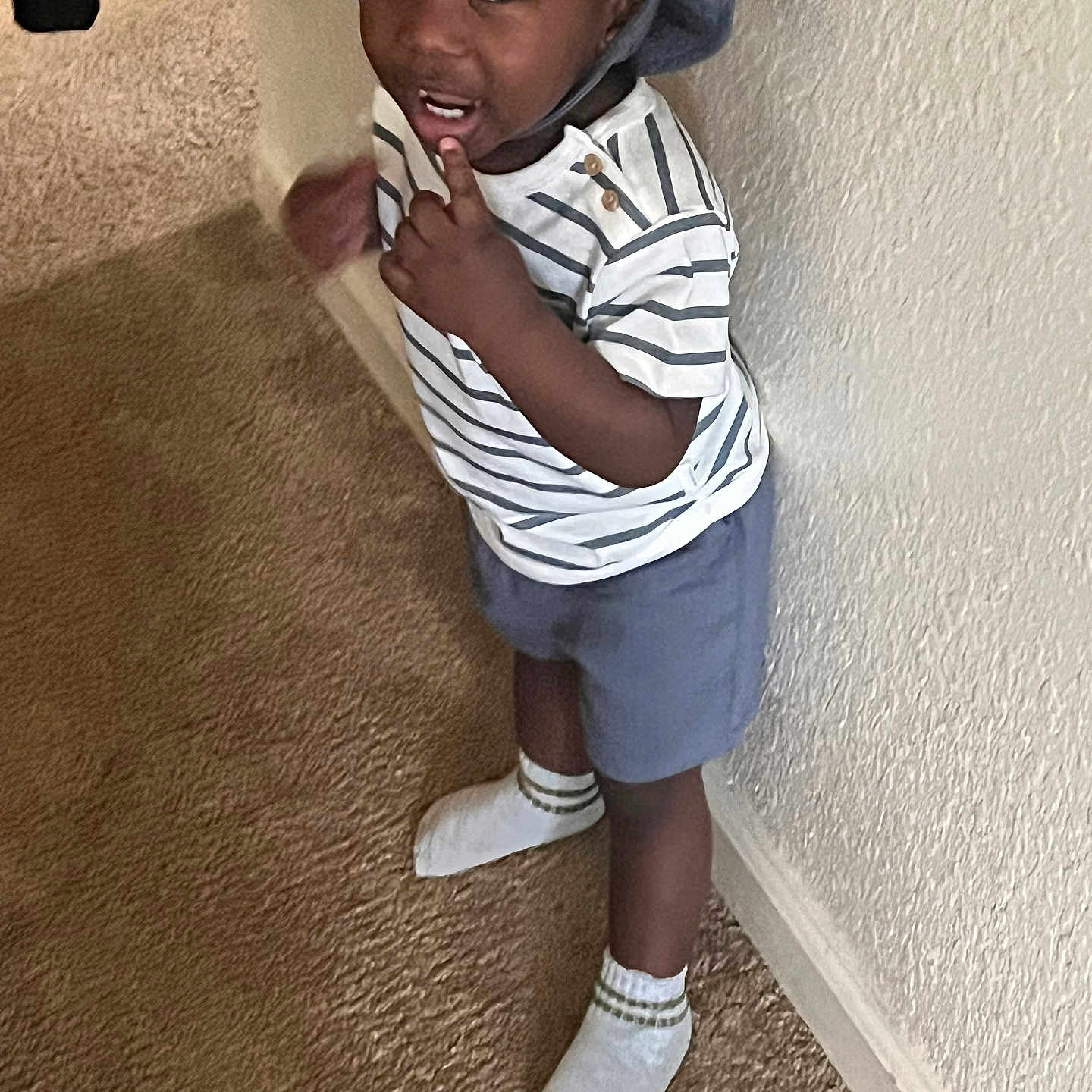 Eeliahom joined the competition — help win amazing prizes! toddler, child, hat, striped_shirt, blue_shorts, socks, carpet, wall, indoor, standing, curious, expression, person, clothing, footwear, casual, young_child, portrait, smiling, cute