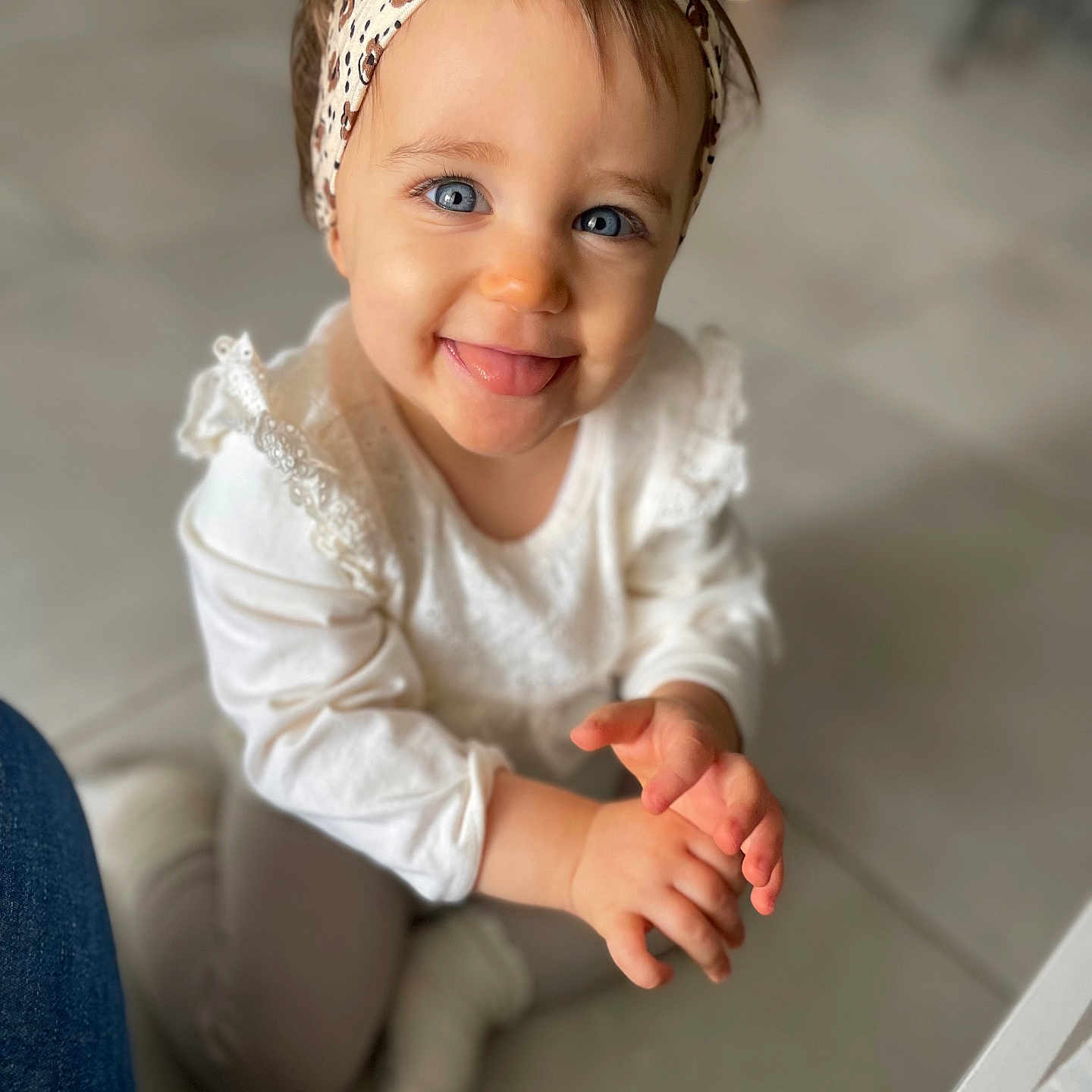 Lèsia a rejoint le concours — aidez-le/la à gagner de superbes lots ! baby, blue_eyes, candid, child, closeup, cute, floor, hands, happy, headband, indoor, infant, person, playful, portrait, sitting, smiling, tongue_out, white_clothing, young_child