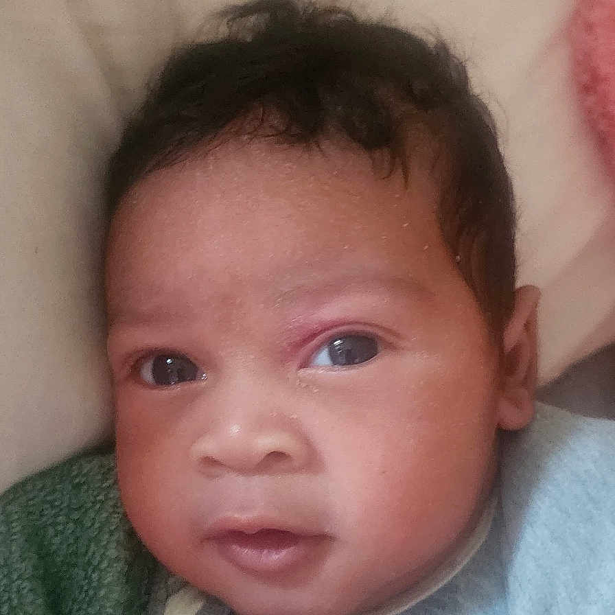 Adonis is registered to the contest to win money with this photo: baby, infant, face, portrait, eyes, blanket, clothing, curly_hair, skin, expression, head, young_child, indoors, cozy, looking, person, cute, newborn, resting, closeup