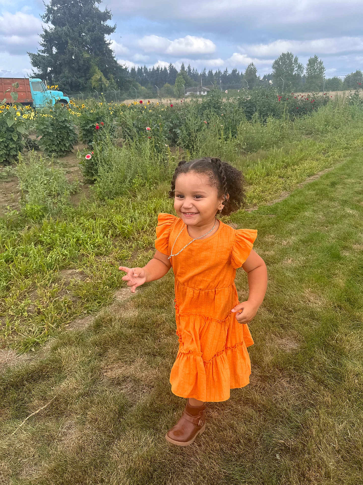 Ixchel is registered to the contest to win money with this photo: child, girl, orange_dress, boots, grass, flower_garden, sunflowers, vintage_truck, outdoor, smiling, curly_hair, nature, daylight, cloudy_sky, rural, greenery, playful, happy, portrait, casual