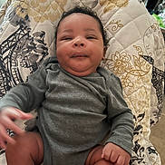 Jkc joined the competition — help win amazing prizes! baby, infant, child, gray_clothing, curly_hair, quilt, patterned_blanket, indoor, cute, smile, skin, face, hand, legs, sitting, cozy, person, young_child, relaxed, home