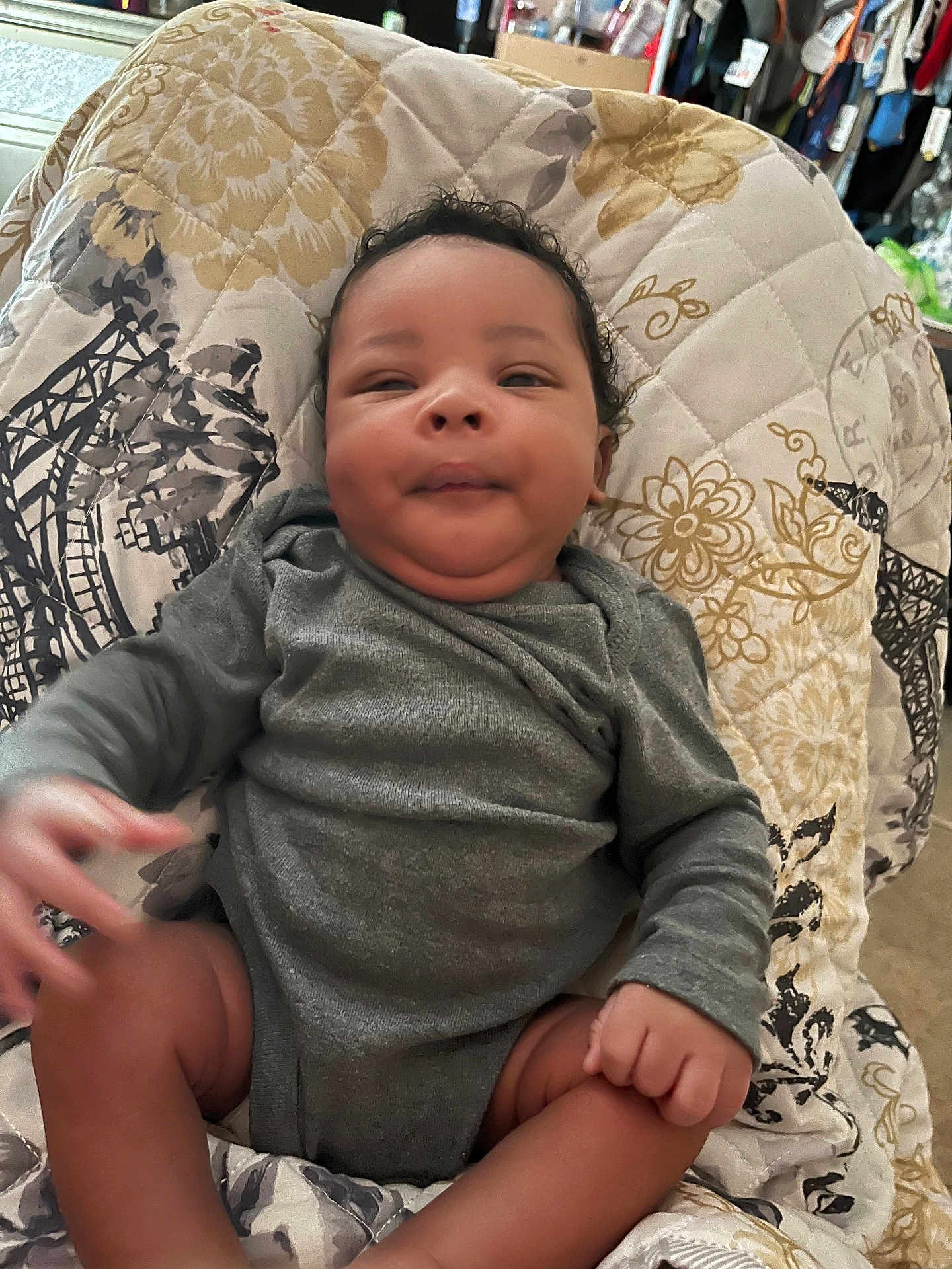 Jkc joined the competition — help win amazing prizes! baby, infant, child, gray_clothing, curly_hair, quilt, patterned_blanket, indoor, cute, smile, skin, face, hand, legs, sitting, cozy, person, young_child, relaxed, home