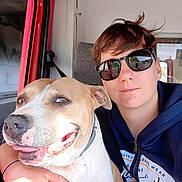 Naya participe au concours pour gagner de l'argent avec cette photo : dog, person, portrait, selfie, sunglasses, smiling, happy, hugging, road_trip, vehicle, car, driver, passenger, seat, window, outdoor, sunlight, brown_and_white, pet, face