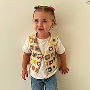 Aliya participe au concours pour gagner de l'argent avec cette photo : child, toddler, smile, curly_hair, hair_bows, colorful_vest, crocheted_vest, white_tshirt, blue_jeans, standing, indoor, plain_wall, happy, casual_clothing, person, cute, young_child, fashion, portrait, small_child