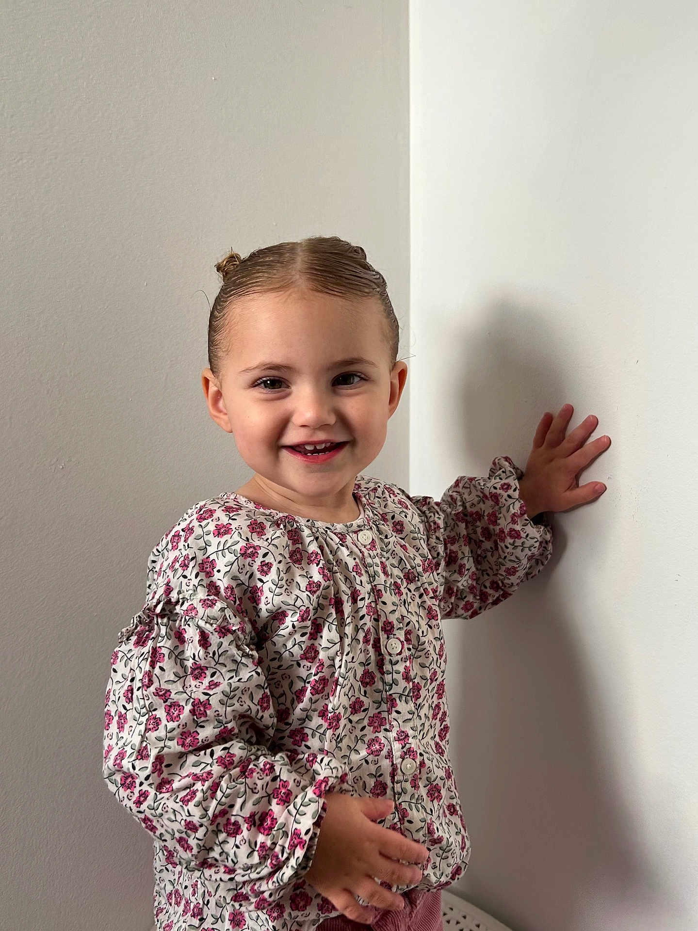 Aliya participe au concours pour gagner de l'argent avec cette photo : buttoned_shirt, casual_clothing, child, cute, face, floral_blouse, hair, hand, happy, indoor, long_sleeves, person, portrait, shadow, skin, smiling, standing, toddler, wall, young_child