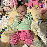 Alyocea is registered to the contest to win money with this photo: baby, infant, child, stuffed_animal, plush_toy, pink_clothing, green_clothing, socks, cushion, bed, blanket, toy, indoor, cute, portrait, seated, expression, face, hands, nursery