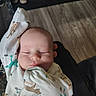 Mateo is registered to the contest to win money with this photo: baby, infant, sleeping, onesie, animal_print, arm_up, cute, peaceful, indoor, floor, wooden_floor, shoes, shoe_rack, hand, face, person, child, newborn, clothing, resting