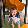 toddler, child, playground, indoor, slide, yellow, netting, barefoot, shorts, tshirt, happy, excited, boy, play, fun, padded_poles, smiling, active, young, casual_clothing