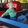 Myles joined the competition — help win amazing prizes! toddler, child, pickup_truck, red_vehicle, keys, green_shirt, jeans, outdoor, autumn, wooden_fence, rustic, daylight, person, vehicle_bed, curious, standing, metal, old_truck, weathered, playful