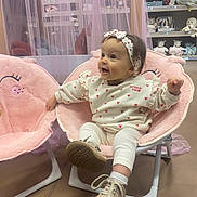 Lyana a rejoint le concours — aidez-le/la à gagner de superbes lots ! baby, child, curtain, cute, fabric, floor, headband, heart_pattern, indoor, infant, person, pink_chair, playful, plush_chair, shelf, shoe, smiling, stuffed_animal, toy_store, white_clothing