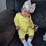 baby, child, yellow_outfit, white_socks, floral_bow, pacifier_clip, strawberry, couch, gray_texture, indoor, cute, infant, smiling, seated, cozy, portrait, person, young_child, happy, comfortable