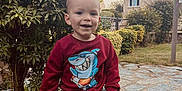 Nolhan participe au concours pour gagner de l'argent avec cette photo : toddler, child, smiling, red_sweatshirt, shark_graphic, bench, stone_bench, garden, bush, tree, house, pathway, grass, outdoors, portrait, hands, sneakers, daytime, happy, casual_clothing