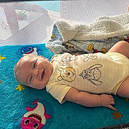 Ellie joined the competition — help win amazing prizes! baby, smiling, infant, onesie, winnie_the_pooh, blanket, blue_blanket, shark_design, plush_toy, cozy, cute, lying_down, happy, child, indoors, soft_texture, playful, colorful, face, person