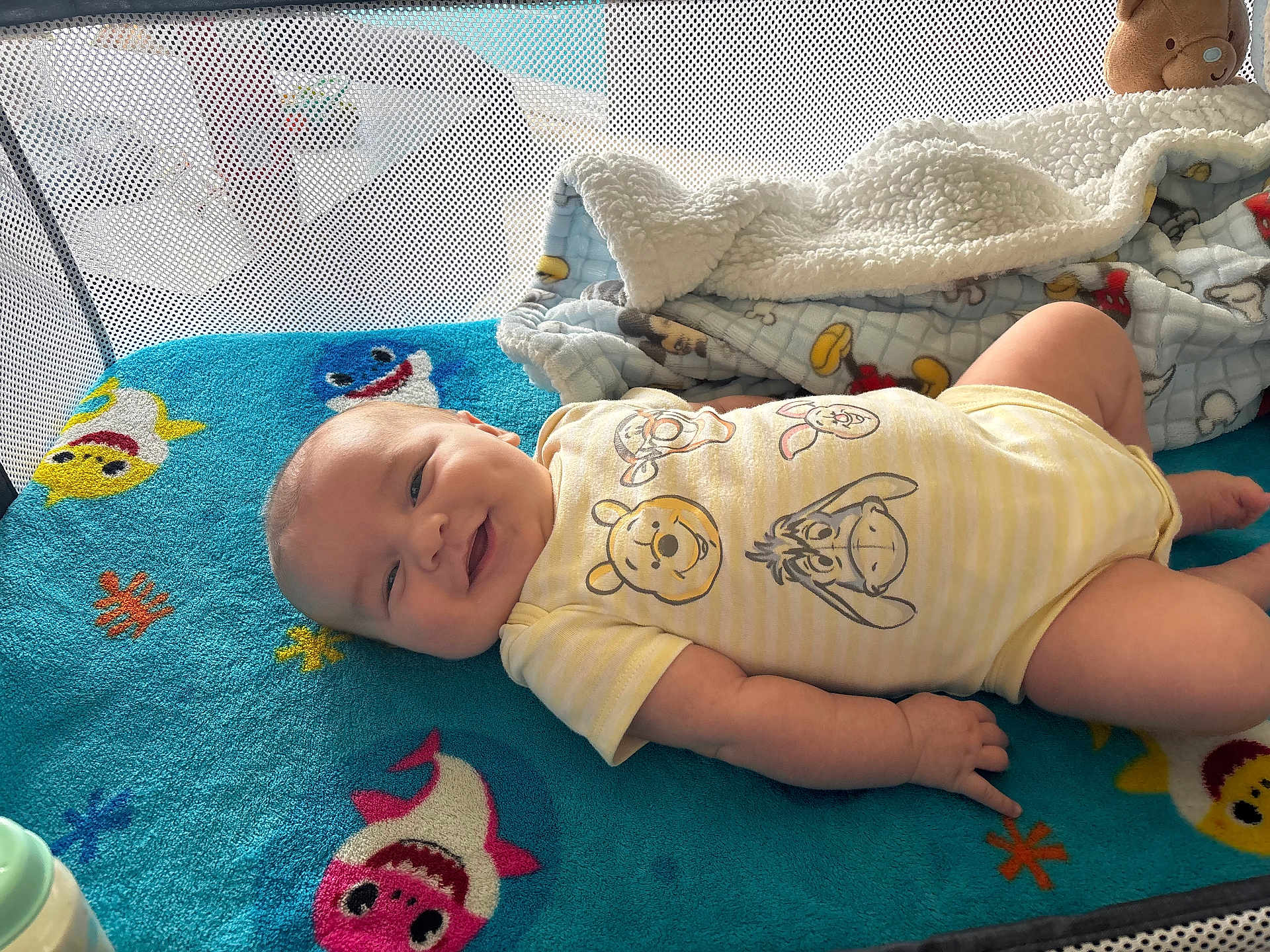 Ellie joined the competition — help win amazing prizes! baby, smiling, infant, onesie, winnie_the_pooh, blanket, blue_blanket, shark_design, plush_toy, cozy, cute, lying_down, happy, child, indoors, soft_texture, playful, colorful, face, person