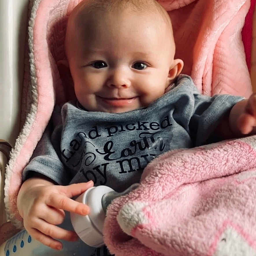 Kaleiah is registered to the contest to win money with this photo: baby, infant, blanket, bottle, smile, face, clothing, cute, child, pink, cozy, sitting, portrait, happy, indoors, soft, warm, newborn, toddler, hand
