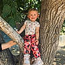 child, toddler, tree, outdoor, nature, leaves, sunlight, pants, shoes, sneakers, smile, person, branch, casual_clothing, daylight, happy, young, cute, playful, park