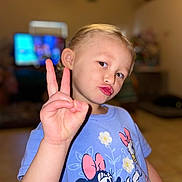Kaleiah is registered to the contest to win money with this photo: child, boy, peace_sign, puckered_lips, blue_tshirt, minnie_mouse, cartoon_characters, indoor, living_room, blurred_background, television, wooden_floor, casual_clothing, short_hair, portrait, cute, playful, person, gesture, expression
