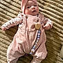 baby, infant, pink_clothing, headband, pacifier_clip, corduroy, blanket, texture, lying_down, cute, child, soft_lighting, indoor, portrait, apparel, footwear, smiling, small_hands, face, cozy