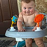 baby, child, infant, smiling, portrait, activity_walker, baby_toy, orange_toy, blue_toy, indoor, door, stone_wall, seated, standing, bare_chested, happy, face, hands, legs, family_photo