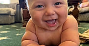 Bowen is registered to the contest to win money with this photo: baby, child, infant, smiling, happy, crawling, portrait, face, eyes, tongue, indoor, living_room, carpet, home, furniture, couch, window, daylight, background_person, close_up