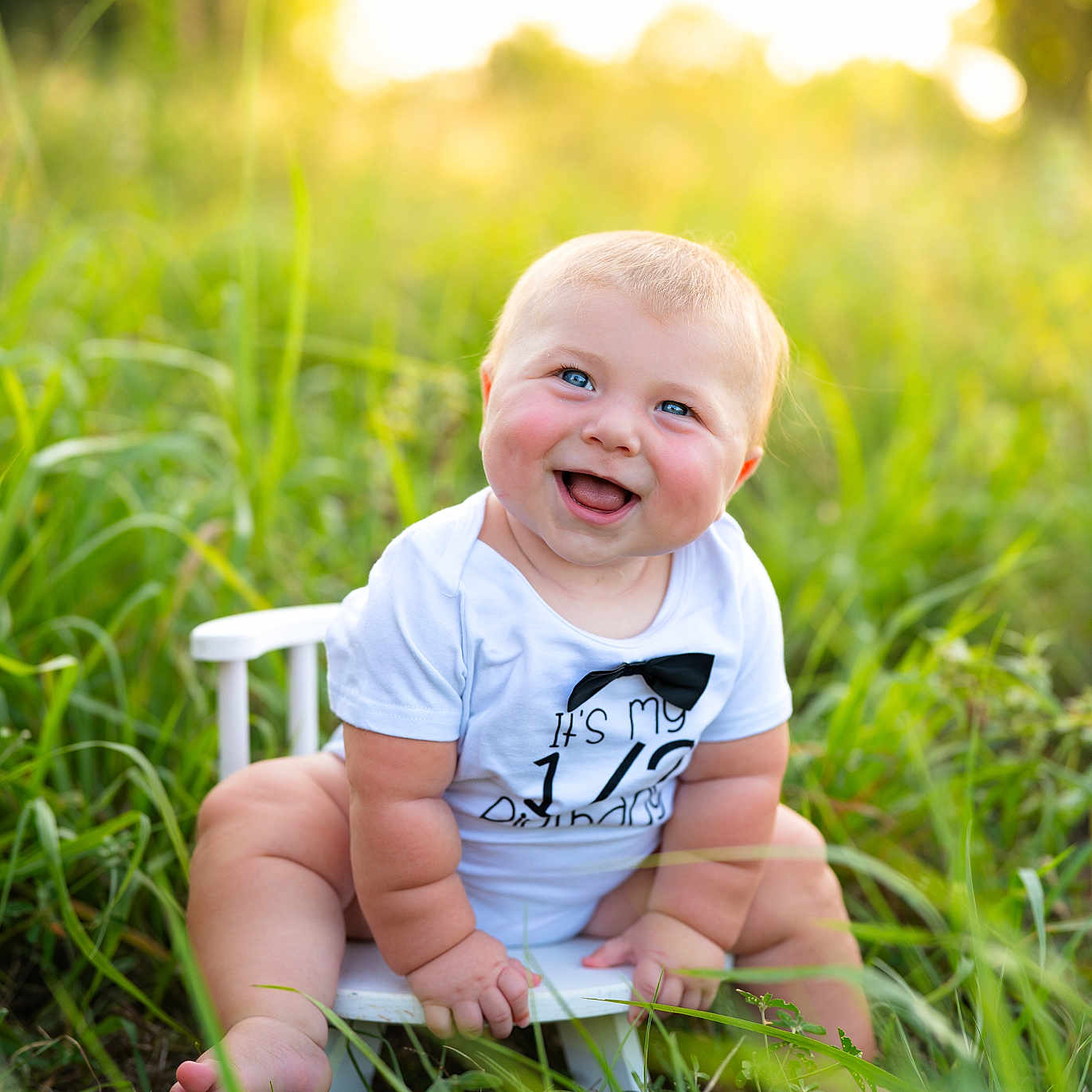 Bowen is registered to the contest to win money with this photo: baby, child, infant, smiling, laughing, portrait, outdoors, meadow, grass, sunset, sunlight, nature, white_chair, seated, blue_eyes, blond_hair, white_shirt, bow_tie, happy, photography