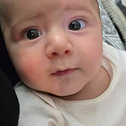 Yasir is registered to the contest to win money with this photo: baby, infant, child, portrait, close_up, face, eyes, wide_eyed, looking_at_camera, indoors, bed, bedding, blanket, clothing, white_outfit, sitting, cozy, home, photography, people