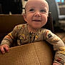baby, infant, child, smile, cardboard_box, pajamas, hand, portrait, indoor, bokeh, blur, face, eyes, happy, cute, grip, wood_floor, chair, home, soft_lighting