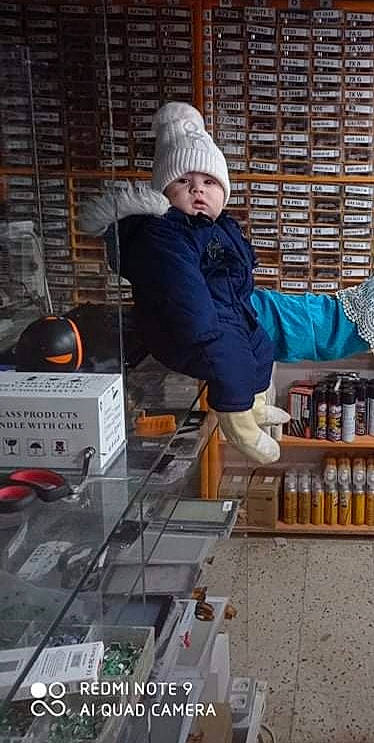 Anes participe au concours pour gagner de l'argent avec cette photo : beanie, boot, box, cap, child, gas, headwear, hoodie, jacket, machine, person, personal_protective_equipment, shelf, sitting, street, street_fashion, winter, workwear
