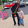Arianna is registered to the contest to win money with this photo: man, child, outdoor, parking_lot, gift_bags, smile, casual_clothing, jacket, glasses, sidewalk, tree, car, asphalt, fun_pose, happy, colorful, people, urban, daytime, cloudy