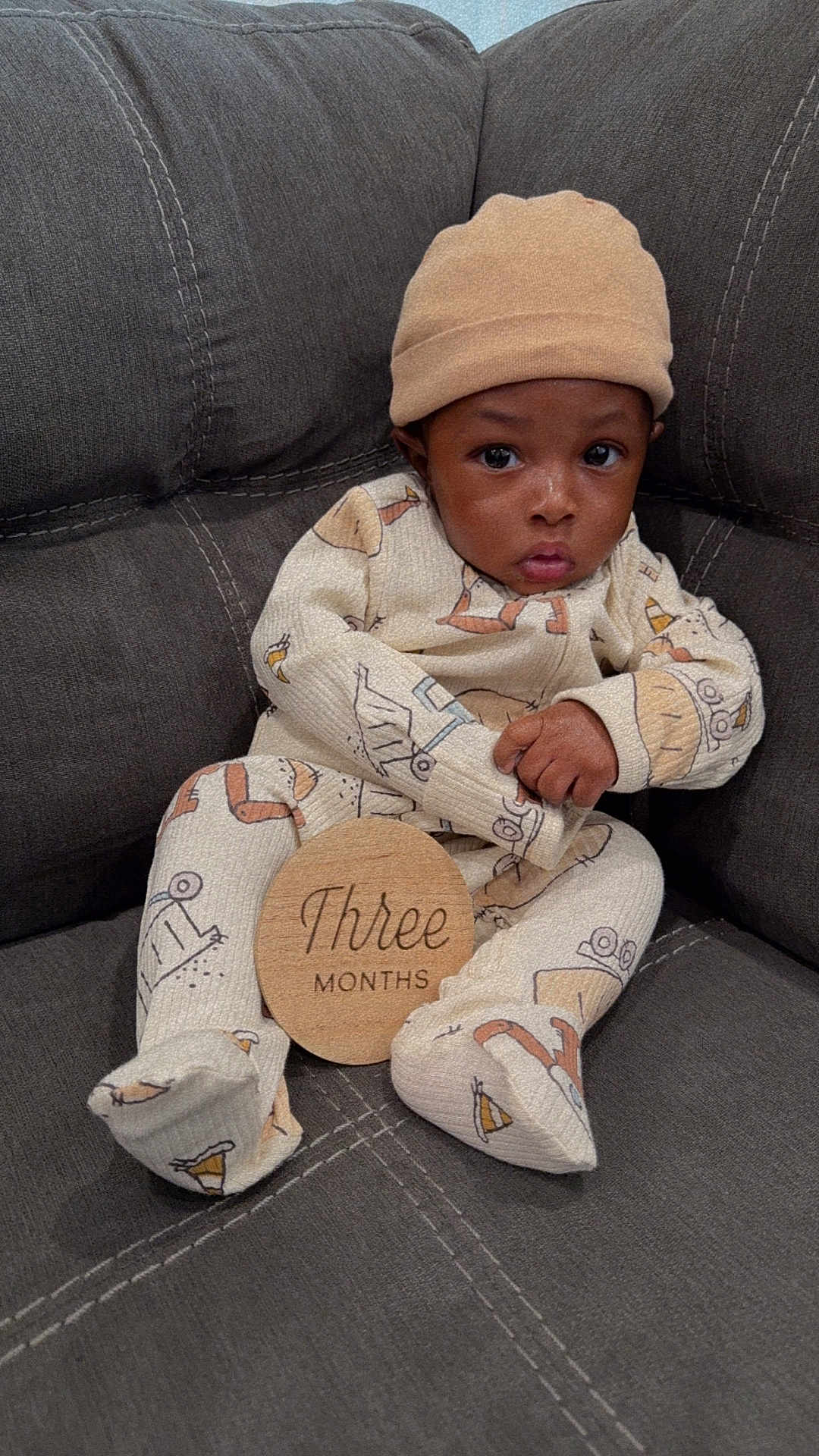 Eastyn is registered to the contest to win money with this photo: baby, infant, child, couch, sofa, onesie, hat, wooden_sign, three_months, sitting, indoor, cute, portrait, cozy, furniture, clothing, person, expression, young, comfortable