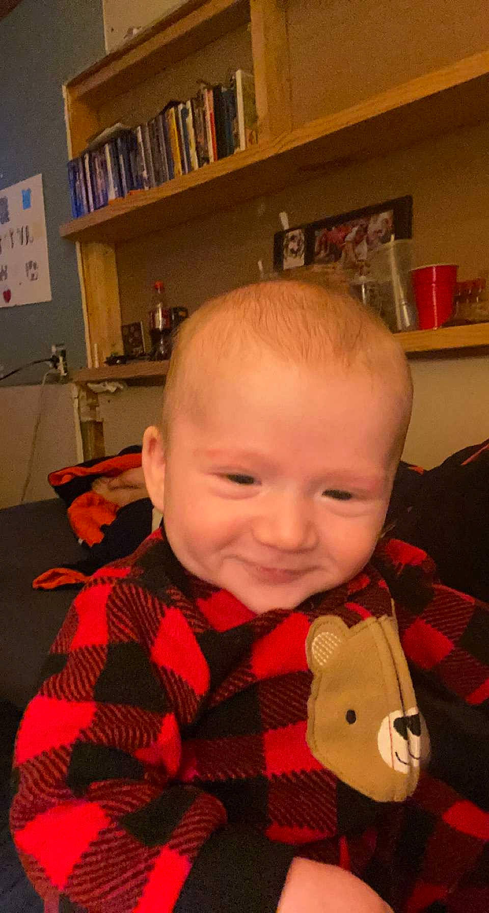 Maverick is registered to the contest to win money with this photo: baby, baby_toddler_clothing, bookcase, cheek, child, collar, face, head, iris, mouth, nose, orange, pattern, person, picture_frame, plaid, shelf, shelving, smile, tartan