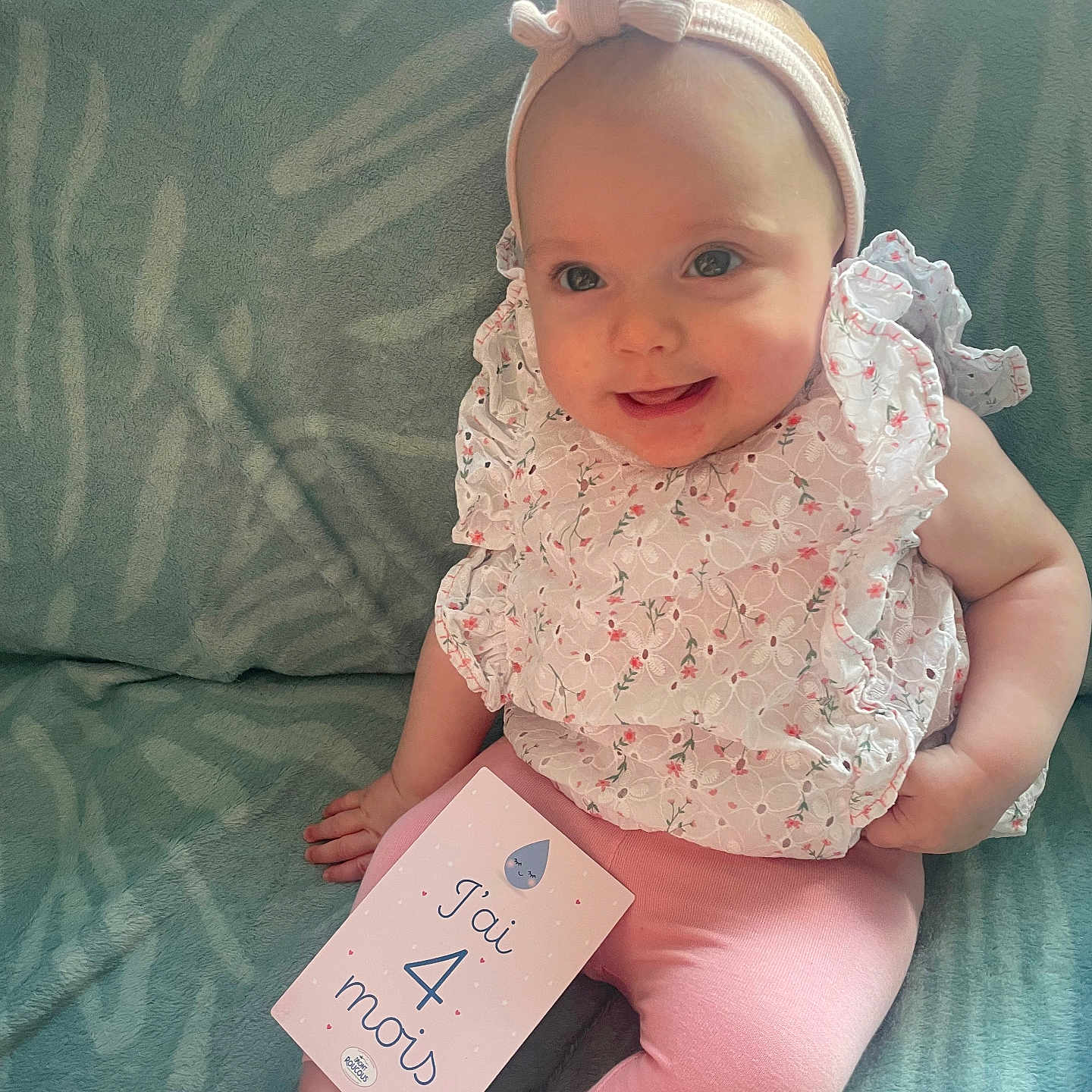 Dana a rejoint le concours — aidez-le/la à gagner de superbes lots ! baby, blanket, child, cozy, cute, feet, floral_top, hand, happy, headband, indoors, infant, legs, milestone_card, pink_clothing, portrait, sitting, smiling, soft_lighting, young_child