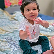 Gianna Paz joined the competition — help win amazing prizes! toddler, child, baby, indoor, bed, clothing, sitting, happy, face, hands, smiling, patterned_bedspread, pants, sock, cute, portrait, person, young_child, home, cozy