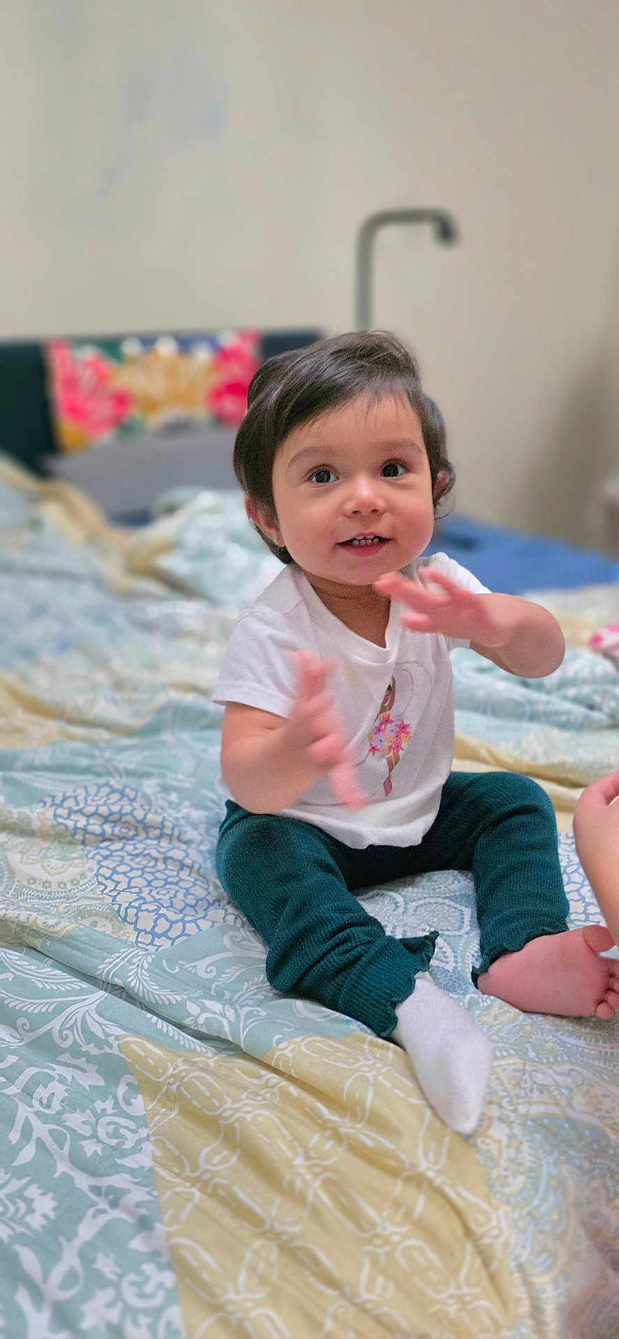 Gianna Paz joined the competition — help win amazing prizes! toddler, child, baby, indoor, bed, clothing, sitting, happy, face, hands, smiling, patterned_bedspread, pants, sock, cute, portrait, person, young_child, home, cozy
