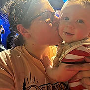 Gavin joined the competition — help win amazing prizes! baby, child, person, woman, glasses, headband, kiss, smile, striped_clothing, holding, indoor, warm_lighting, close_up, affection, human_face, love, parent_and_child, blurred_background, people, ring