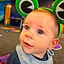 baby, child, headband, green, frog, eyes, face, indoor, playroom, carpet, curious, clothing, cute, infant, portrait, young_child, expression, soft_lighting, closeup, fun