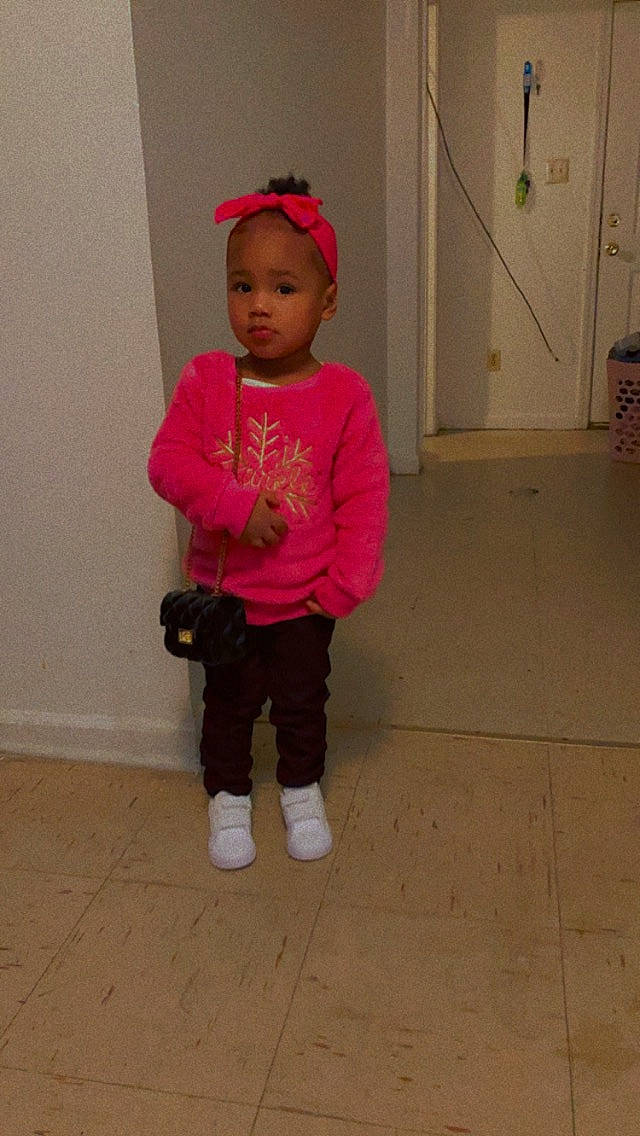 Alexis is registered to the contest to win money with this photo: baby, baby_toddler_clothing, child, clothing, door, face, fashion_accessory, floor, flooring, happy, hardwood, head, headgear, magenta, person, pink, sleeve, sock, t_shirt, toddler