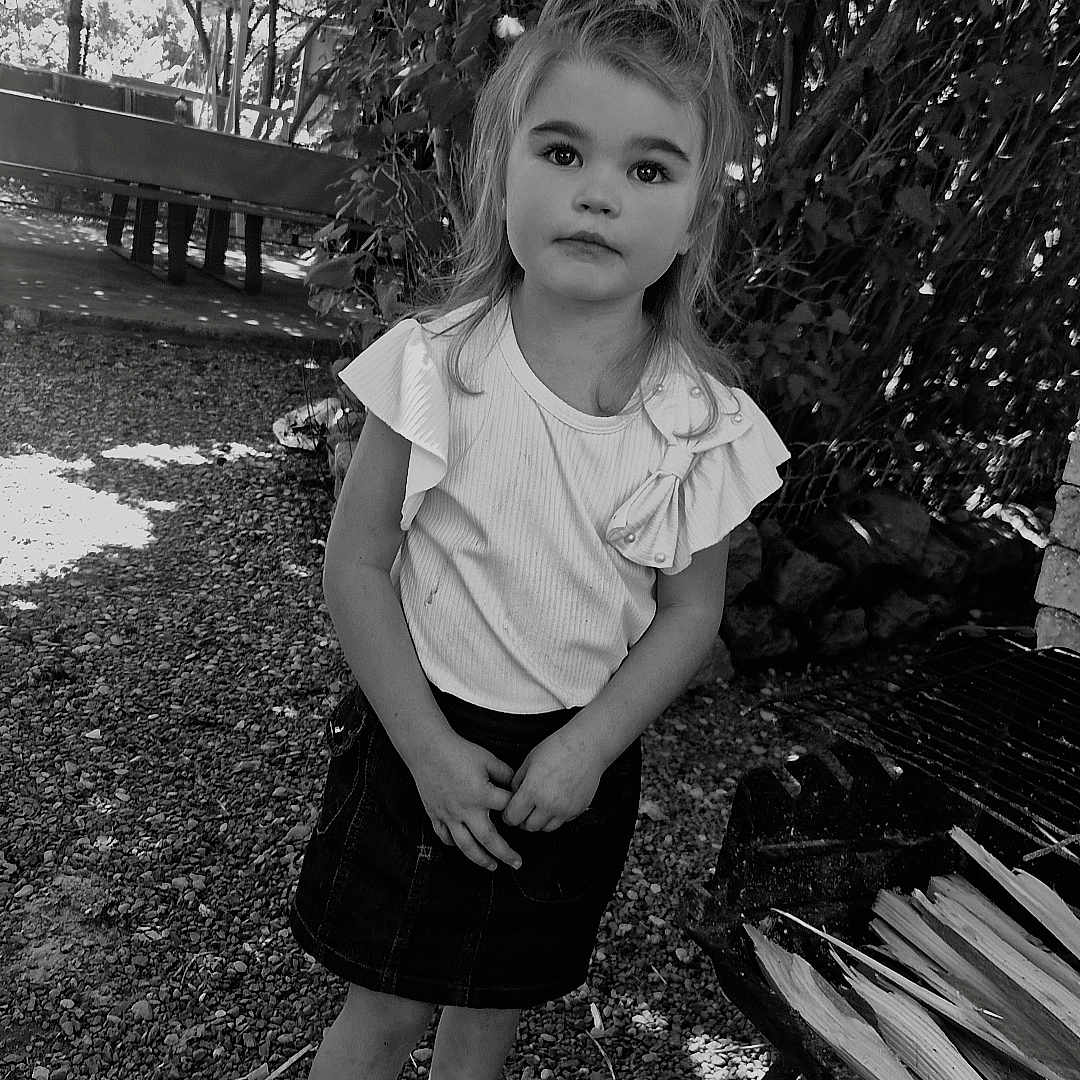 Kylianna a rejoint le concours — aidez-le/la à gagner de superbes lots ! bow, casual_clothing, child, curious_expression, daylight, girl, gravel, grill, hands_clasped, leaves, nature, outdoor, portrait, skirt, sneakers, standing, tree, white_top, wood, young