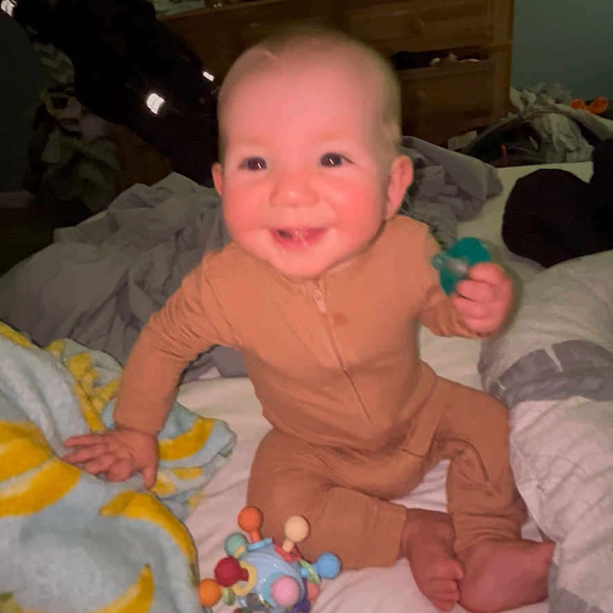 Elijah joined the competition — help win amazing prizes! baby, child, smiling, bed, blanket, toy, indoor, onesie, person, happy, face, furniture, television, dresser, home, infant, cute, sitting, playful, room