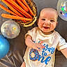 Elijah joined the competition — help win amazing prizes! baby, infant, smiling, onesie, carrots, basket, balloons, celebration, birthday, happy, laying_down, cute, child, face, person, indoor, colorful, food, festive, fun
