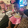 bed, birthday, chair, child, cute, desk, fingers, floor, footwear, indoor, leopard_print, minnie_mouse_ears, person, pink_clothing, polka_dot, room, sitting, television, thoughtful, toddler