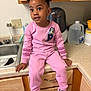 child, pink_clothing, kitchen, countertop, wooden_cabinet, sink, curious, sitting, shoes, indoor, portrait, person, casual, smiling, young_child, home, appliance, water_jug, playful, cozy