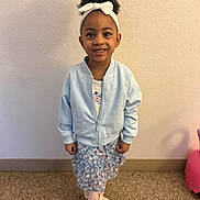 Jhordyn is registered to the contest to win money with this photo: child, girl, smile, headband, bow, jacket, dress, floral_pattern, slippers, socks, indoor, wall, carpet, standing, portrait, hair, afro, eyes, happy, toy