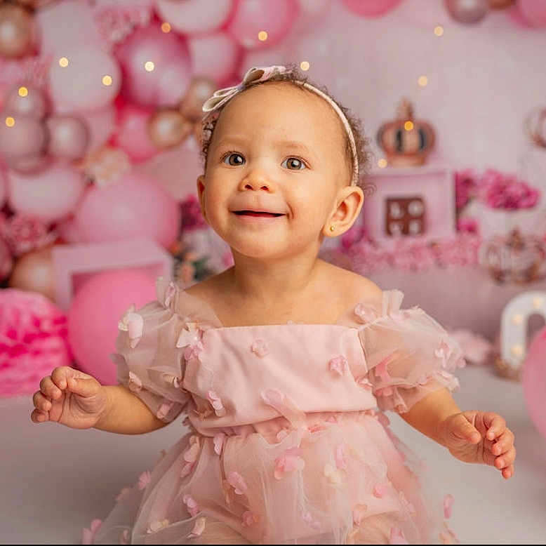 Paris Jayde is registered to the contest to win money with this photo: background, balloons, birthday, celebration, child, cute, decoration, face, festive, girl, happy, headband, indoors, joy, party, pink_dress, portrait, smiling, soft_lighting, toddler