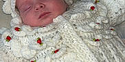 Maeve joined the competition — help win amazing prizes! baby, sleeping, crocheted_clothing, white_outfit, red_roses, blanket, floral_pattern, infant, cute, peaceful, soft_texture, handmade, knitted, face, headwear, newborn, portrait, resting, indoors, adorable