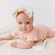 Maeve joined the competition — help win amazing prizes! baby, infant, child, headband, bow, ribbed_clothing, peach_outfit, blanket, soft_texture, lying_down, curious_expression, chubby_cheeks, indoor, portrait, cute, smiling, person, young_child, skin, eyes