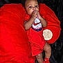 Kashmir is registered to the contest to win money with this photo: baby, black_background, child, curly_hair, cute, eyes, face, four_months, hands, indoors, infant, lying_down, newborn, nike_logo, pillow, portrait, red_clothing, socks, sucking_fingers, wooden_sign