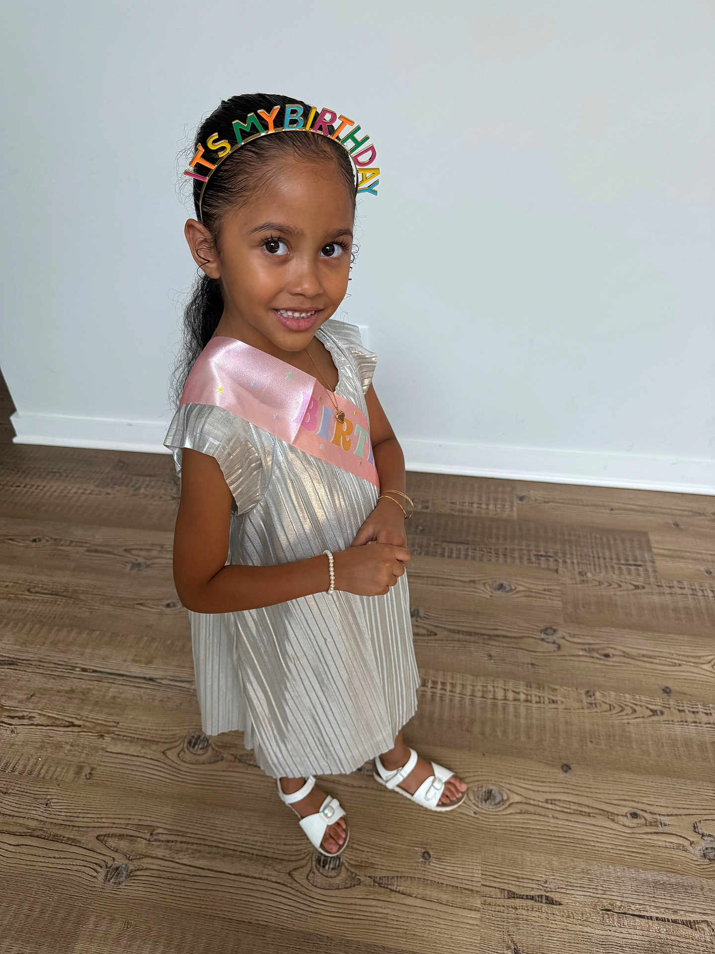 Hayliana is registered to the contest to win money with this photo: child, girl, birthday, headband, dress, silver_dress, sash, smile, standing, wooden_floor, white_sandals, bracelet, party, celebration, happy, indoors, person, cute, holiday, fashion