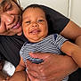 Michael is registered to the contest to win money with this photo: baby, striped_onesie, smiling, adult, holding, closeup, face, skin, hand, love, affection, portrait, indoor, comfort, happy, family, bond, person, candid, expression
