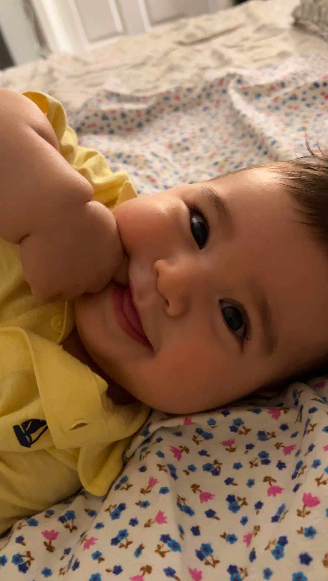 Leon joined the competition — help win amazing prizes! baby, child, smile, face, hand, yellow_shirt, blanket, floral_pattern, lying_down, close_up, cute, happy, indoors, skin, portrait, infant, young_child, soft_lighting, comfort, cozy